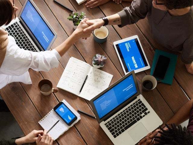 Image of multiple laptops and mobile devices spread out on a table with people using them.
